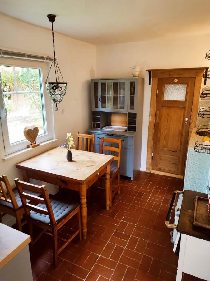 Küche des Ferienhauses mit Holztisch, Vitrine und Blick in den Garten