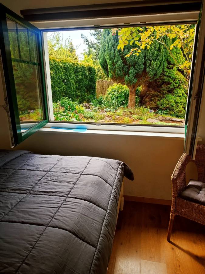 Doppelbett am geöffneten Fenster mit Blick in den Garten